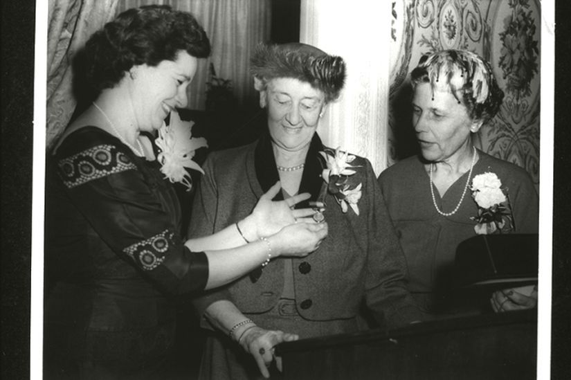 woman showing two ladies in formal wear a medal