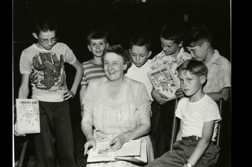 A woman signing a book surrounded by young boys.