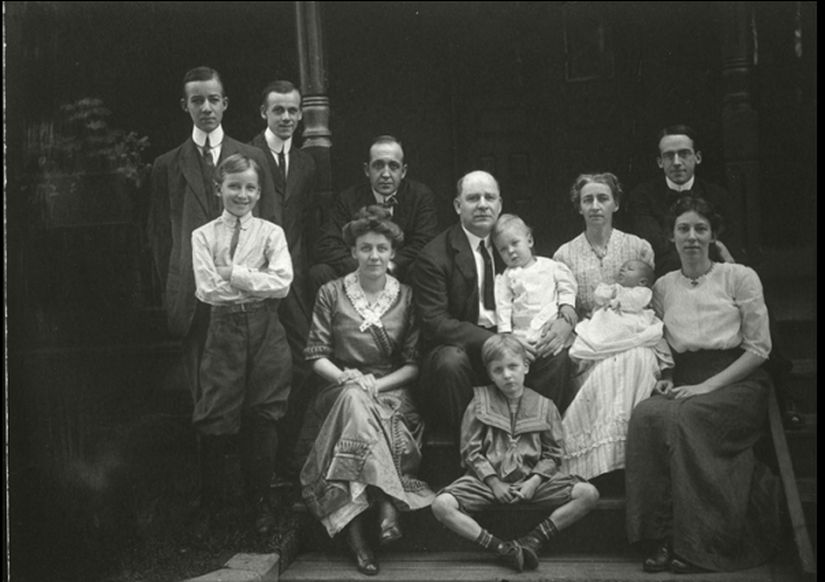 Family portrait with 12 individuals of varying ages on the front steps of a porch.