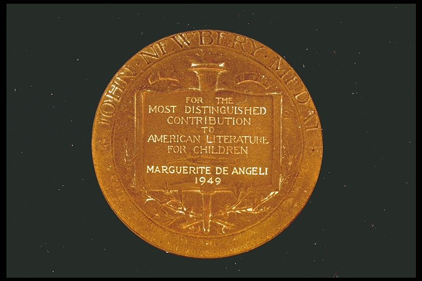 Image of a round gold medal with the words: John Newbery Medal along the top of it andin the middle of it are the words: "For the most distinguished contribution to American Literature for children. Marguerite de Angeli 1949."