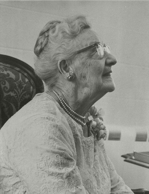 The profile of an older woman with glasses sitting in a chair.